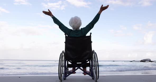 Woman with arms outstretched on wheelchair at beach 