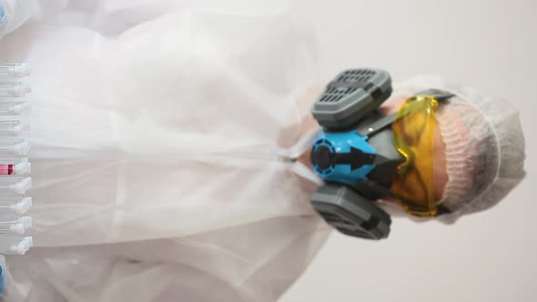 Vertical Video. A Doctor in a White Coat and Protective Mask Shows a Test Tubes Holder and Looking alt