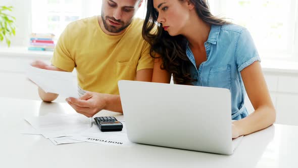 Worried couple calculating their bills with laptop in the kitchen alt