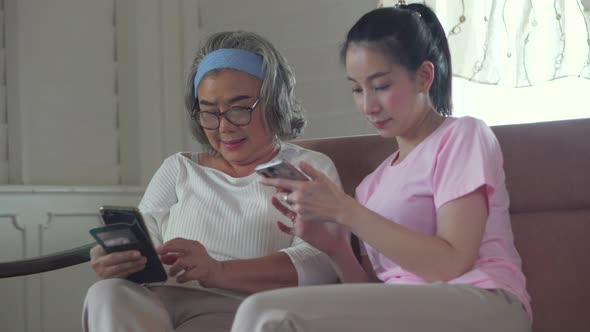 Senior asian mother and middle aged daughter using mobile smart phone in living room