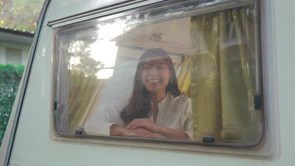 cheerful young woman waiving saying hello at window of a camper RV van motorhome alt