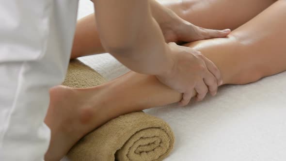 Professional therapist giving relaxing Thai oil leg massage treatment to a woman in spa