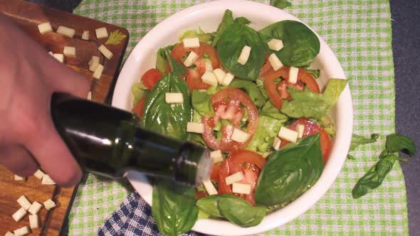 Hands making a lettuce and tomato with basil, adding olive oil in a white bowl alt