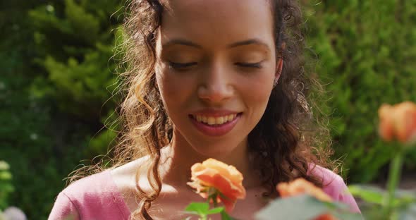 Portrait of happy biracial woman smelling roses in garden alt