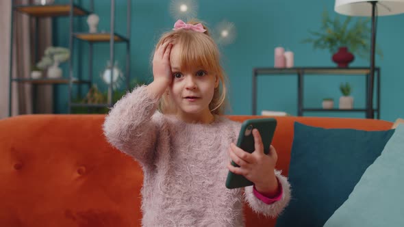 Excited Amazed Winner Kid Girl Use Mobile Phone Say Wow Yes Raising Hands in Surprise Alone at Home alt