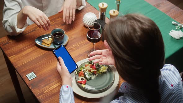 Woman Using Smartphone with Blue Screen and Eating Vegetable Salad Qr Code with Online Menu in Cafe alt