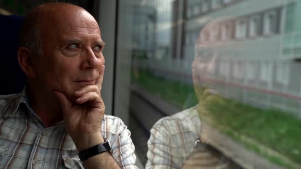 an Elderly Bald Man with Shaggy Eyebrows Rides a Suburban Train. He Rests His Chin on His Hand and alt