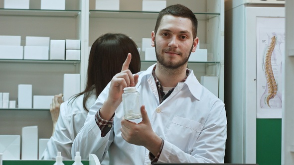 Young malepharmacist holding a white blank bottle of pills