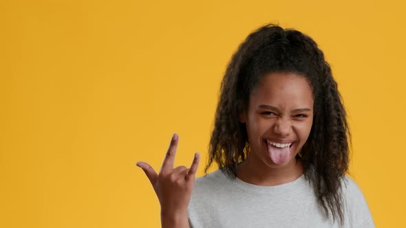 Black Teenager Girl Gesturing Rock Sign Showing Tongue Yellow Background alt