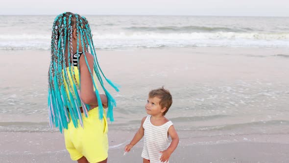 A Boy in a Striped Tshirt is Dancing to the Music with His Sister African Braids on the Beach Near alt