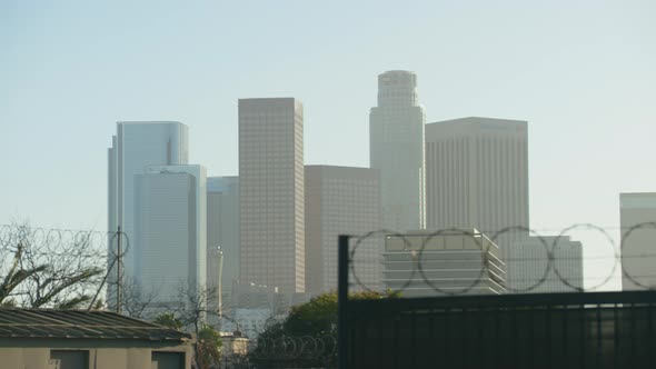 Skyscrapers of Los Angeles seen behind a barb wire sliding gate (daytime) withing traffic in the for alt