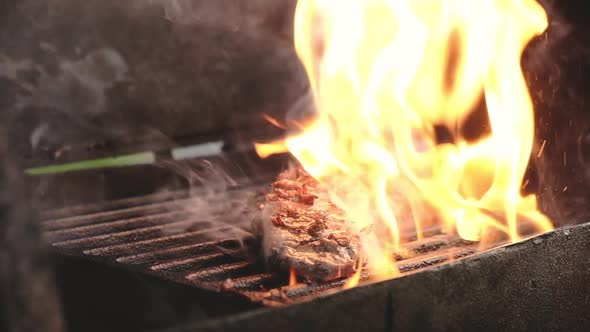 cook roasts meat on charcoal grill in flame of  fire and turns steaks on grill alt