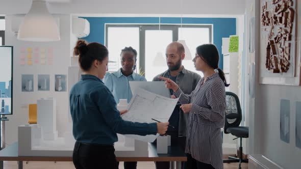 Multi Ethnic Group of Architects Working with Blueprints and Building Model on Table alt