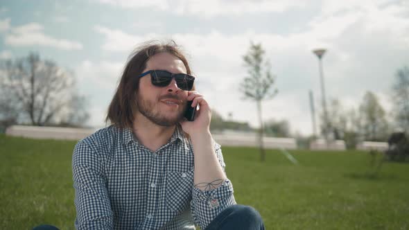 Fashion Macho Smiling with Smartphone in Casual Sweatshirt. Happy Guy in Hood Talk on Mobile Phone alt