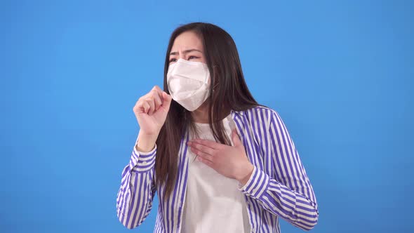 Beautiful Young Asian Woman with a Protective Medical Mask on Her Face Coughs While Standing on a alt