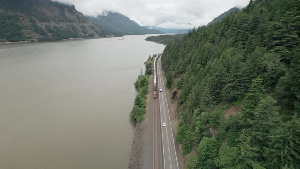 Freight train, traffic along Columbia River travels towards camera, reverse aerial dolly. alt