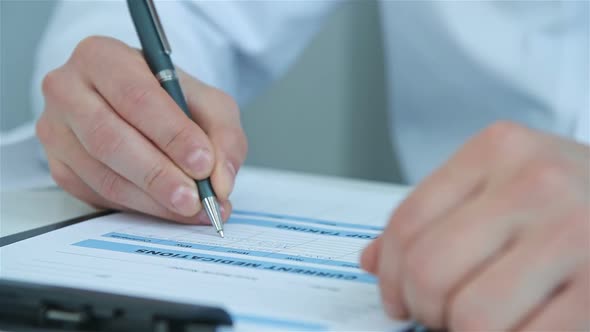 Male Doctor With Pen Writing Medical Report