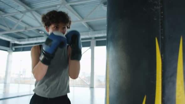 Fit Young Boxer Training with Punching Bag Wearing Protective Gloves Indoors in Gym alt