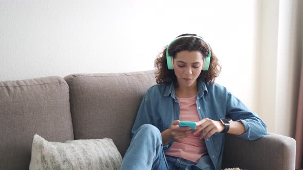 Hispanic Young Woman in Earphones Using Smartphone App Sitting at Home alt