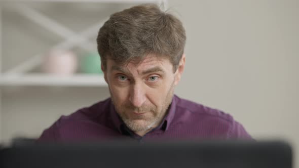 Closeup Portrait of Handsome Middle Aged Man Adjusting Shirt and Hair Sitting at Laptop Indoors alt