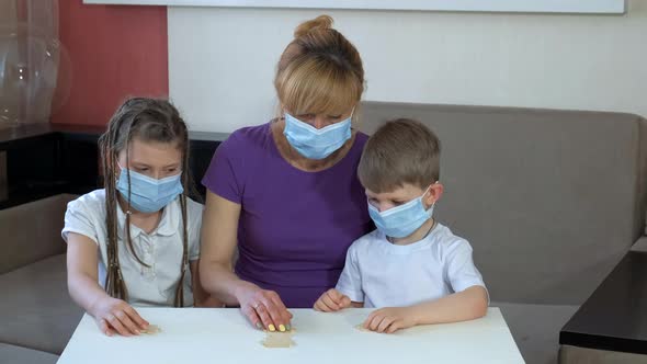 Mother and Children in Medical Masks Put Together Wooden Puzzles in the Room