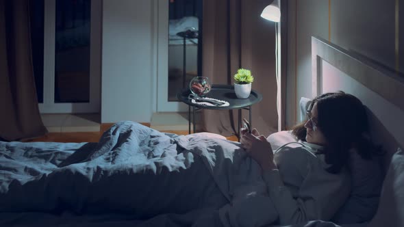 Girl Lies at Night in Her Bed with a Mobile Phone alt