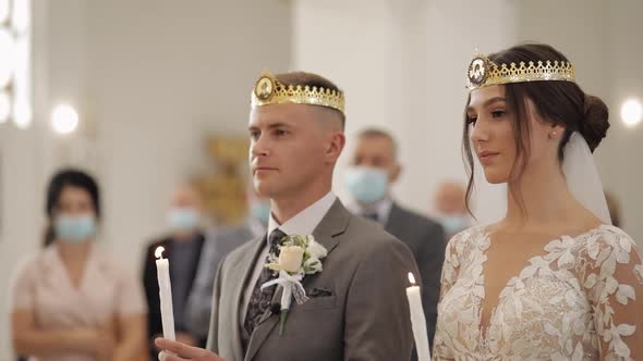 Newlyweds ceremony caucasian bride groom stand in church, holding candles in their hands alt