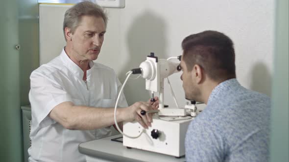 Elderly Female Ophthalmologist and Male Client Checking Eyesight in Clinic alt