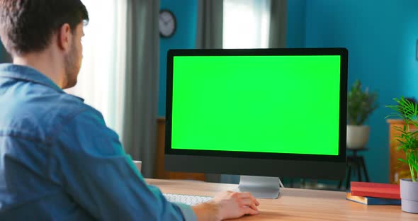 Man Uses All in One Computert with Green Mockup Screen While Sitting at the Desk alt