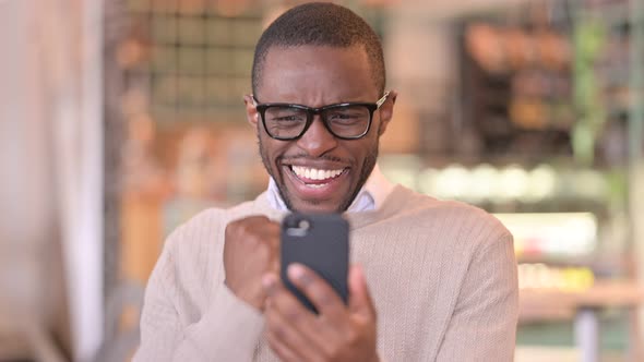 Portrait of Excited African Man Celebrating Success on Smartphone  alt