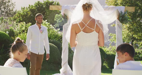 Caucasian bride walking to outdoor altar to groom and wedding officiant alt