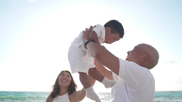 Side View of Happy Asian Man Holding Excited Boy Up in Sunset Sunrays As Cheerful Woman Laughing at alt