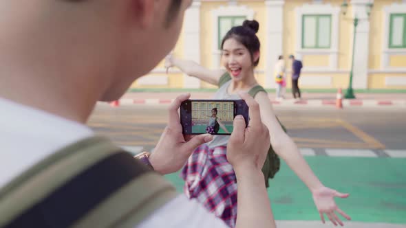 Young couple using mobile phone taking photo each other near street while spending holiday trip alt