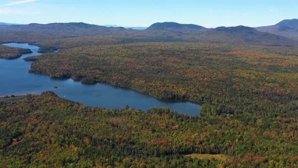 Aerial drone shot tilting down over a serene blue mountain lake in the forest along a mountain range alt