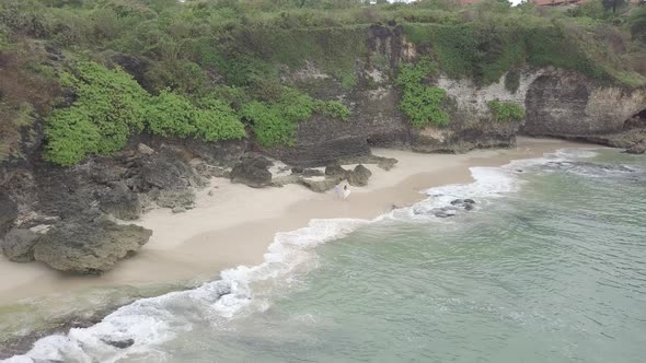 Aerial bride and groom running on white sand secret beach Bali Indonesia paradise island rocky cliff