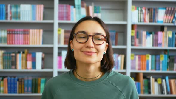 Closeup Portrait of a Young Woman Student Against the Background of Bookshelves in the University alt