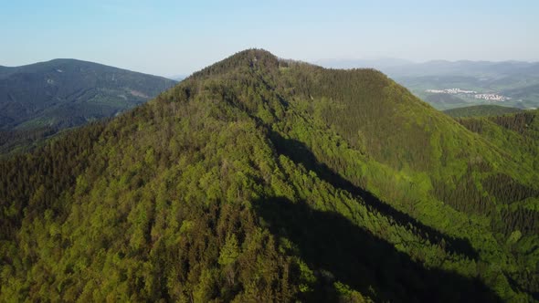 Aerial View of Dense Green Forest in Steep Hills the Horizon Shows a Distant City in the Valley