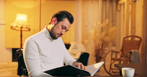 Young Handicapped Man Reading Book Sitting in Wheelchair at Home Room Front View of American alt
