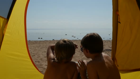 Two Boys Sitting Inside the Tent and Admiring the Sea