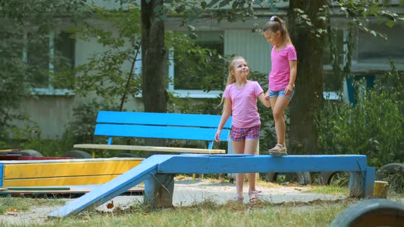 Two girls play in the Playground on a summer day. The elder sister helps the younger