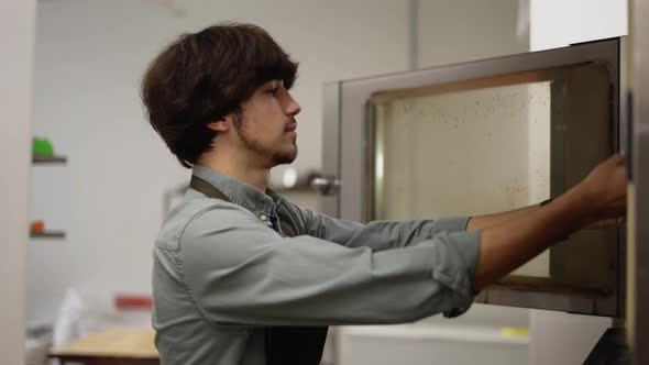 Male Cook Opening the Oven and Putting Uncooked Pie on the Kithen alt