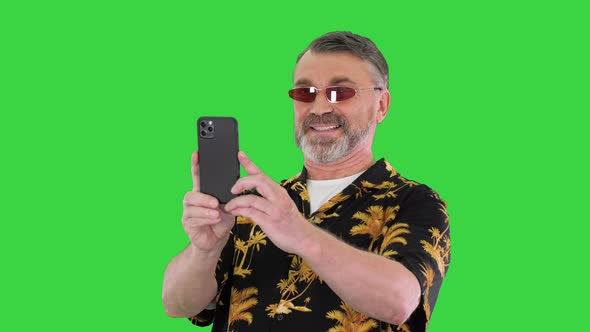 Senior Man Wearing Loud Hawaiian Shirt Photo with Mobile Phone on a Green Screen Chroma Key alt