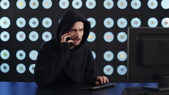 Male Hacker Wearing Black Hoodie Types on Keyboard Answers Call Feels Relieved