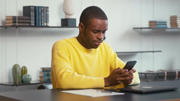 Young man surfs the internet in a smartphone at the desk alt