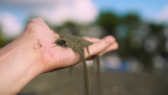 close-up hand grabs a handful of dry sand and lets it fall between his fingers alt