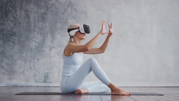 Young and sporty girl in sportswear is doing exercises at home using virtual reality helmet. alt