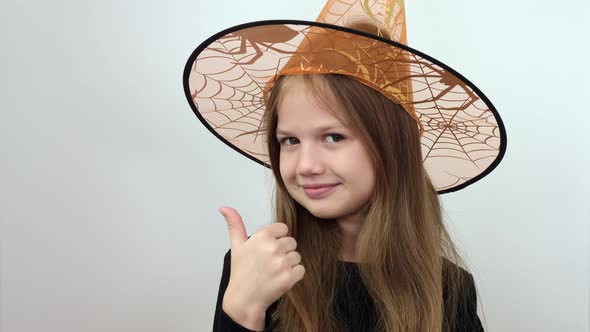 Little Girl in Orange Witch Hat Showing Up Big Thumb and Demonstrating Sign of Satisfaction alt