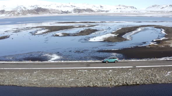 Car Driving Along a Narrow Road Over a Lake in Winter Conditions alt