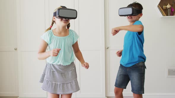 Caucasian brother and sister gesturing while wearing vr headset at home alt