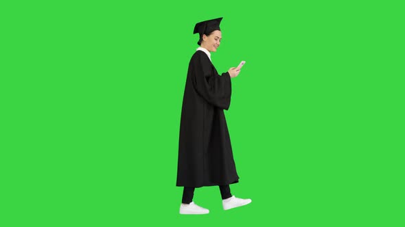 Smiling Female Graduate in Mortarboard Texting on Her Phone While Walking on a Green Screen, Chroma alt